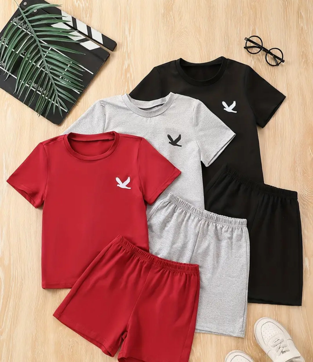 Boys 6-Piece Eagle Graphic Print T-Shirt and Shorts Set laid out on a wooden surface, featuring colorful short-sleeve T-shirts in red, gray, and black, along with matching shorts, perfect for casual summer wear.